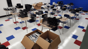 Classroom with boxes full of binders and desks covered with an assortment of office supplies